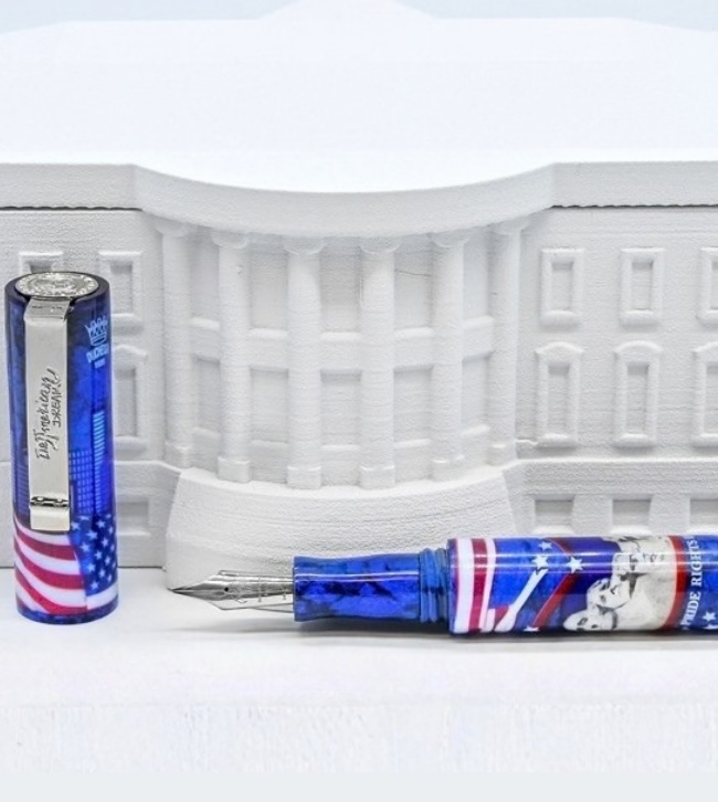 La stilografica The American Dream in palladio su acciaio, cappuccio in piedi accanto al corpo con pennino, decorata con bandiera americana e skyline di New York, davanti alla Casa Bianca in modellino bianco